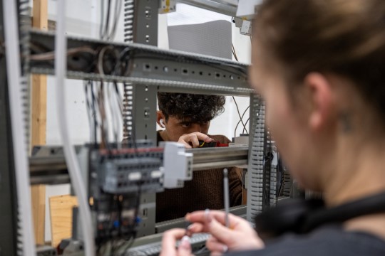 En jente og en gutt som jobber på hver sin side av et elektrisk anlegg.