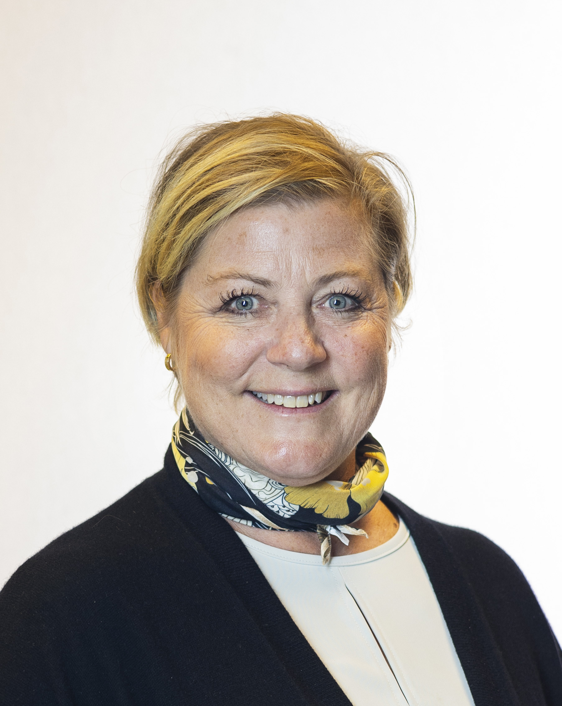 Dame med kort, blondt hår. Tørkle i halsen og sort dressjakke.