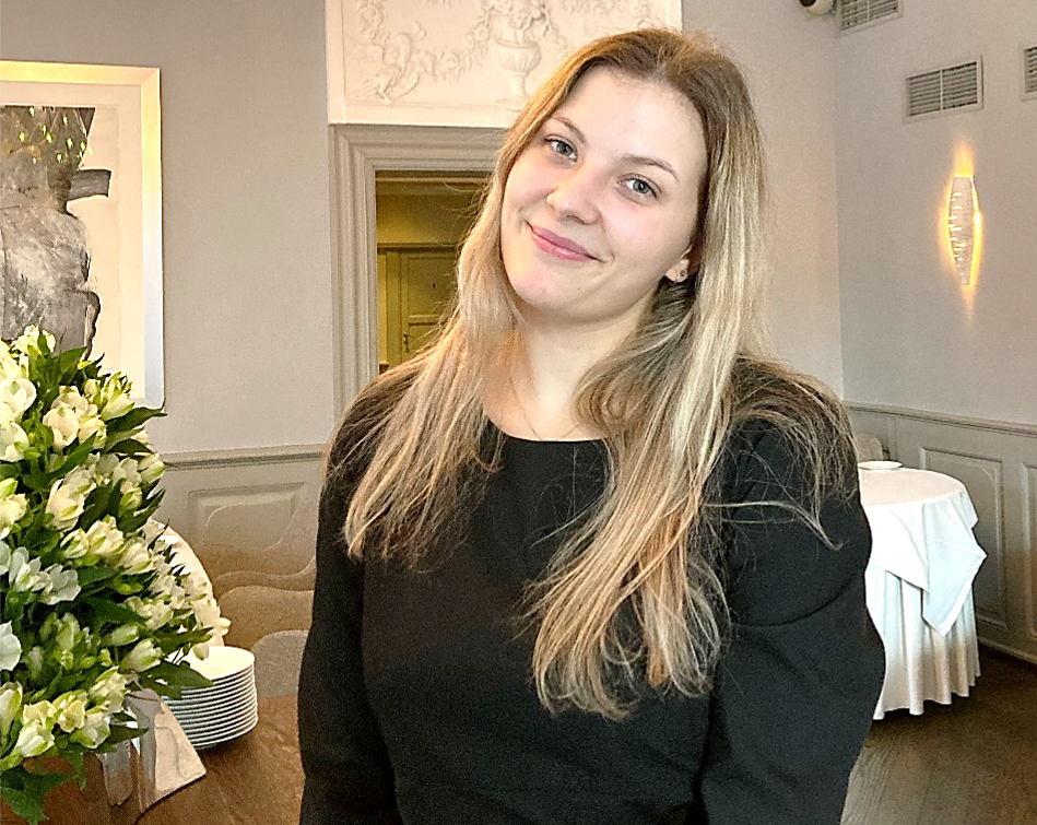 Ung kvinnelig servitør står inne i en restaurant, med hodet på skakke.