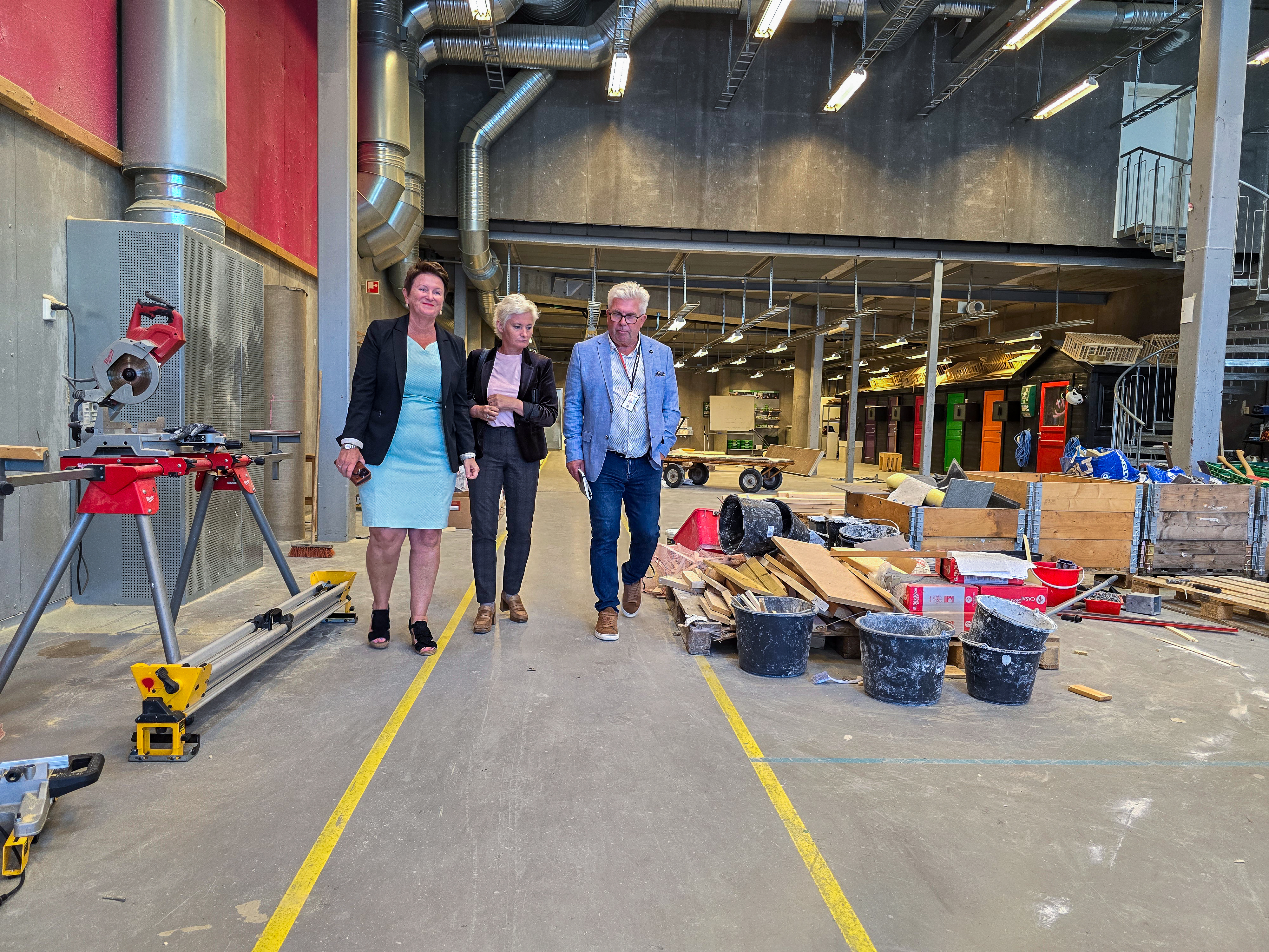 rektor, fylkesordfører og avdelingsleder går i verkstedet blant planke og byggematerialer.