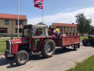 Traktor med henger, pyntet med ballonger og flagg, i kortesje med elever og lærere.