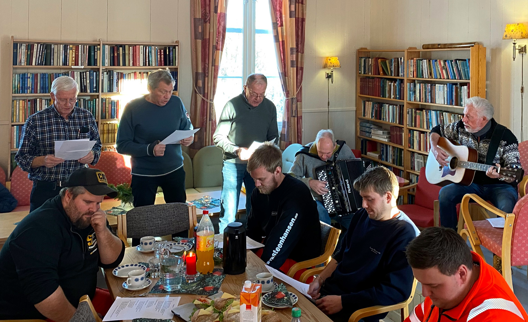 Tre menn fra Stavdal grendelag står og synger, en mann sitter på høyre side og synger. Fire menn sitter rundt bort i forgrunnen.