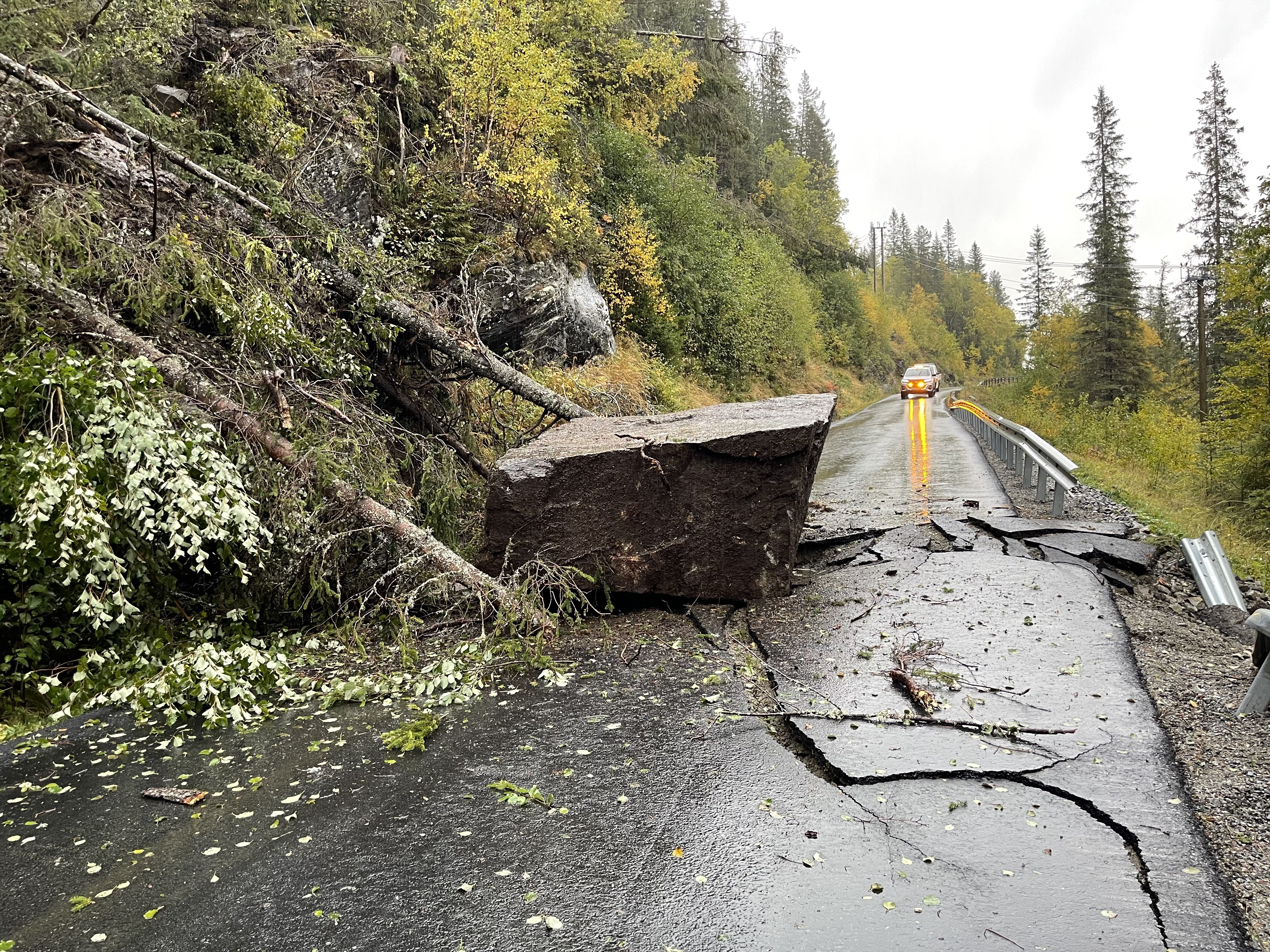 Veibanen forsvinner innover i bildet. Steinblokk og trær ligger i bildets venstre side, asfalten på høyre sider har store sprekker og skader.