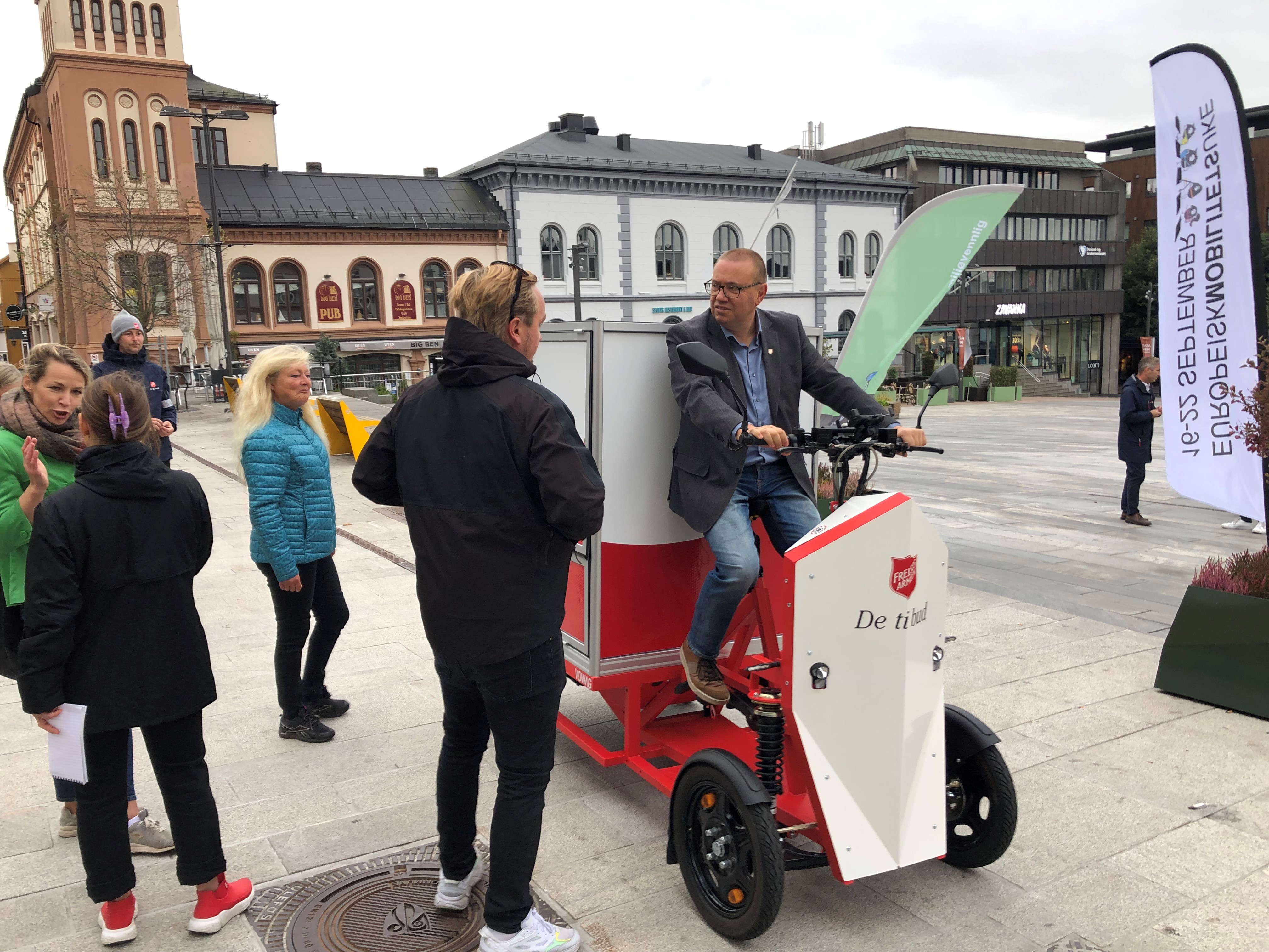 Mennesker på torget i Tønsberg står rundt og betrakter varesykkel med kasse bakpå.