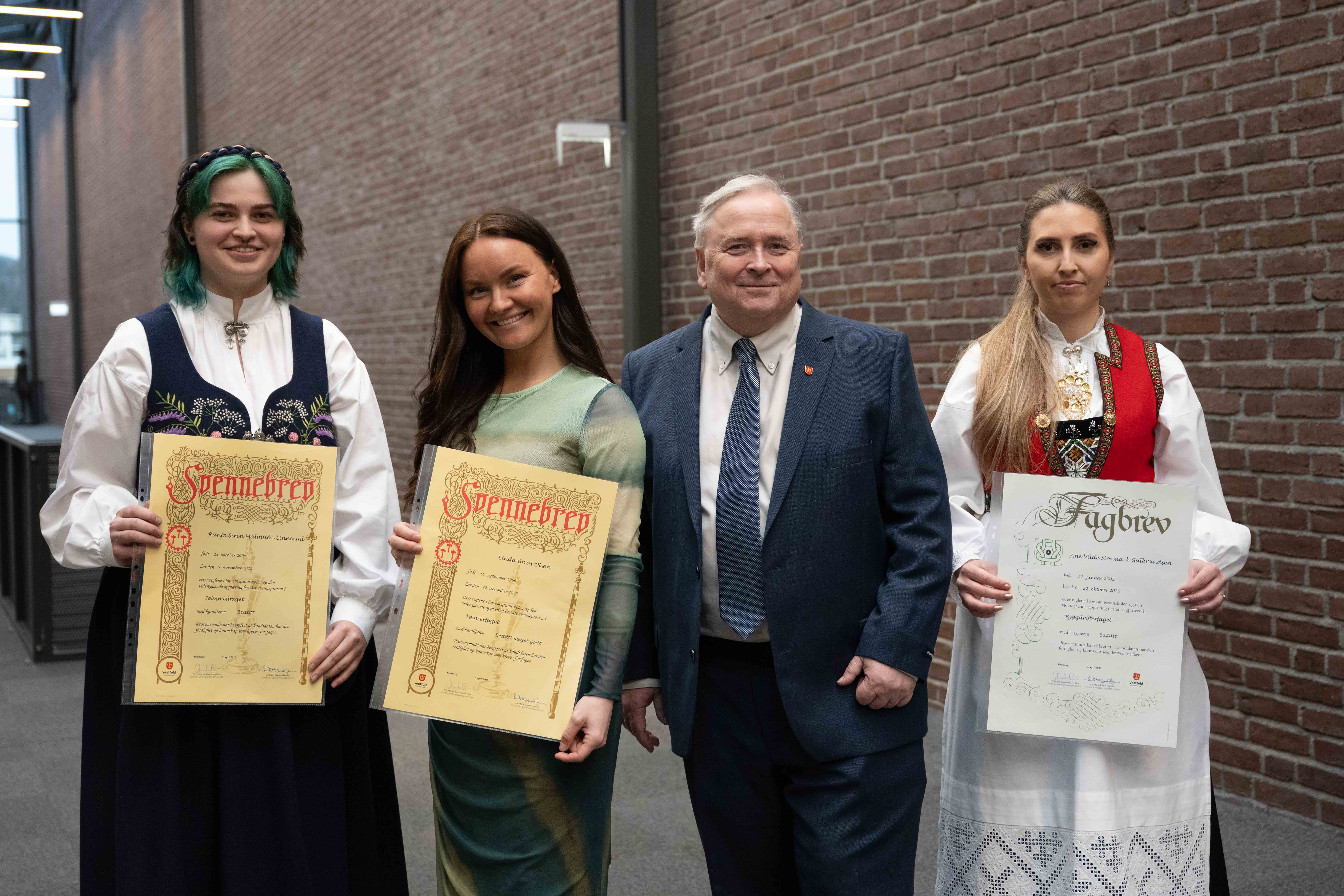Tre jenter med diplom står rundt en mann i dress.