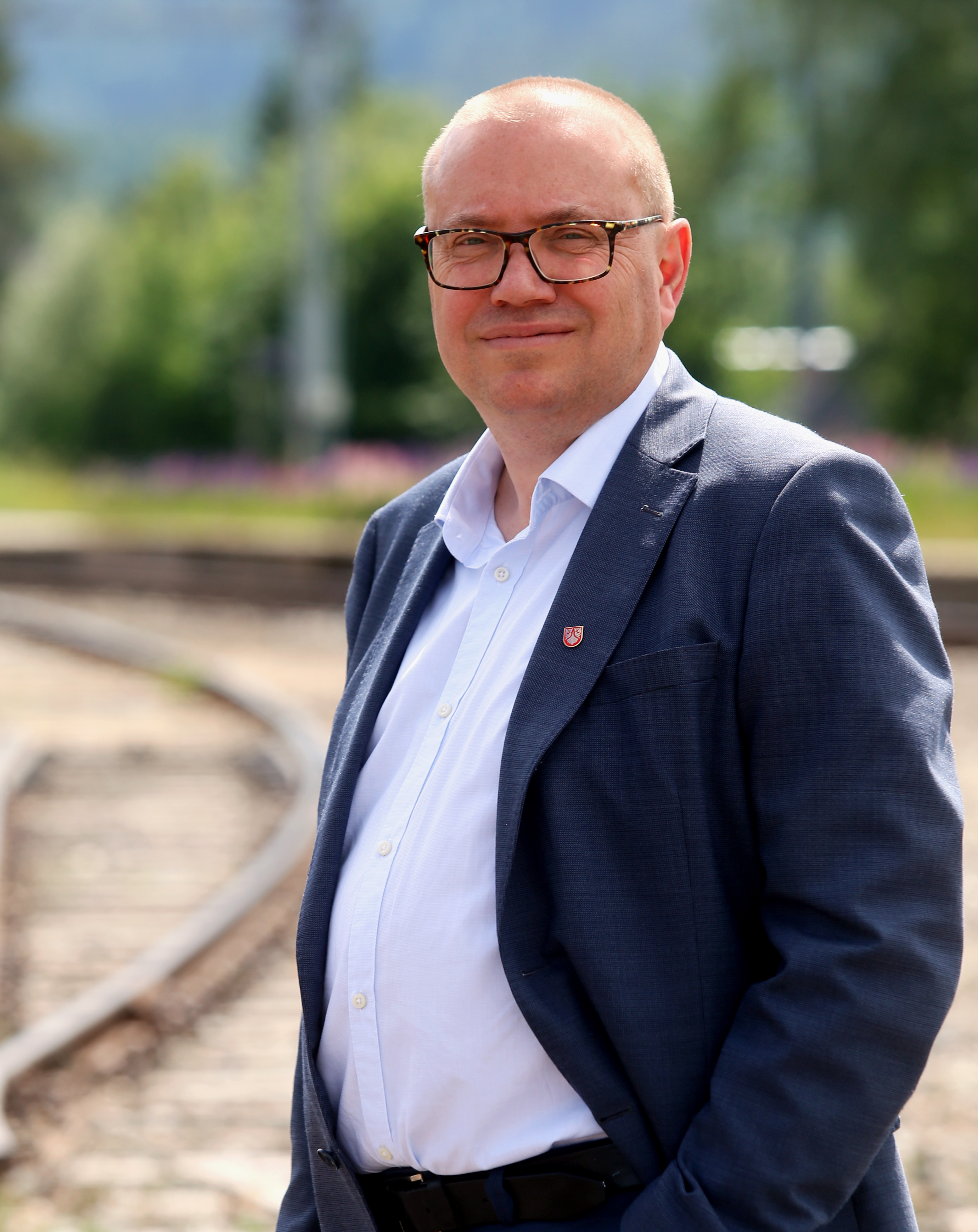 Portrett av mann, utsnitt fra livet og opp. Jernbanespor i bakgrunnen.