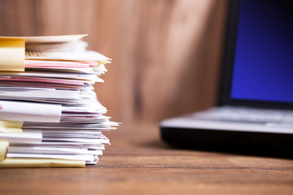 Foto av papirbunker med PC i bakgrunnen