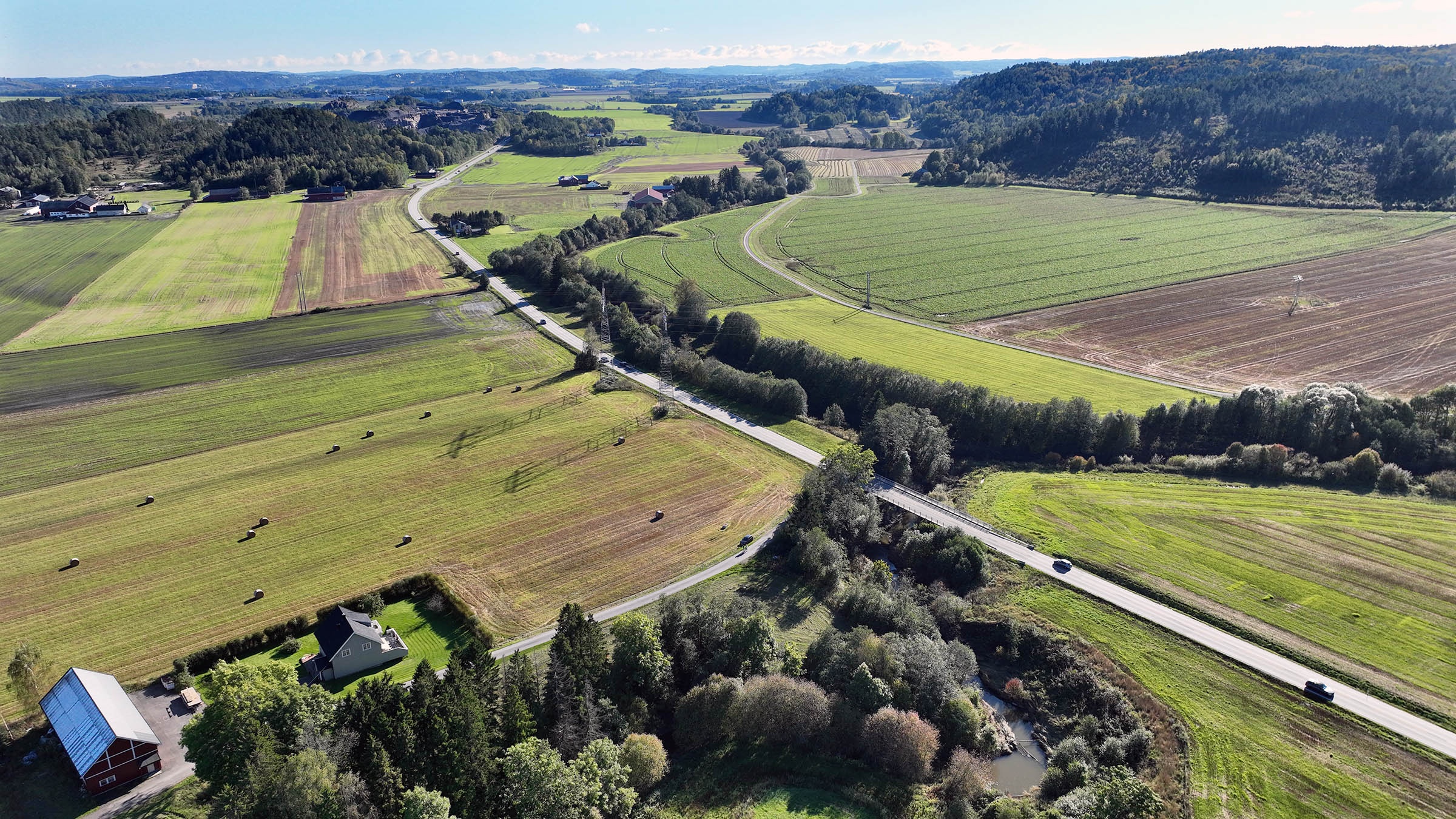 Dronebilde som tatt sørover mot Ås som viser fv.35, Bispeveien. Velseelv i forgrunnen der den nye brua skal krysse elva.