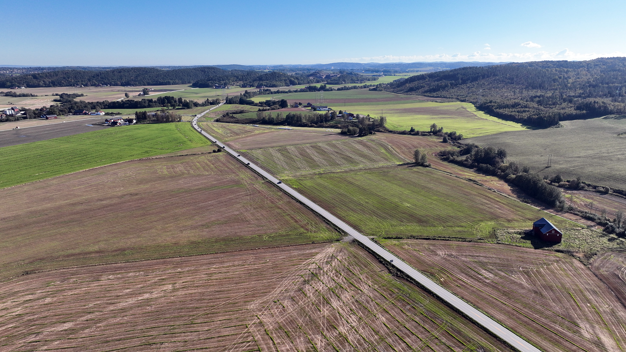 Stort dronebilde som viser Bispeveien fv.35 omgitt av jorder. Bildet er tatt fra Vivestad mot Ås.