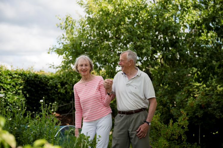 Eldre ektepar som holder i hånd ute i en hage