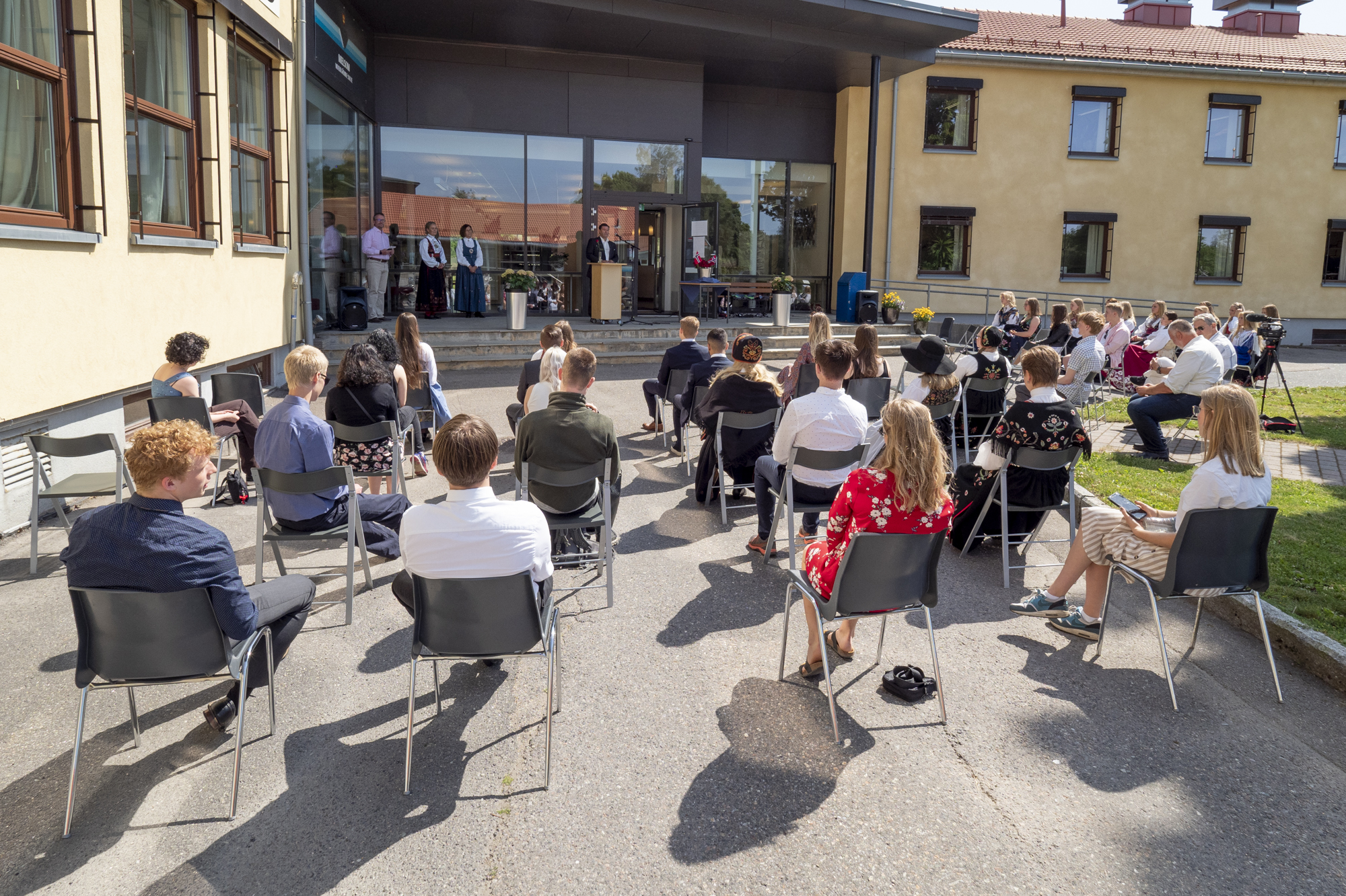Rektor holder tale på tunet mens elever sitter på stoler og lytter.