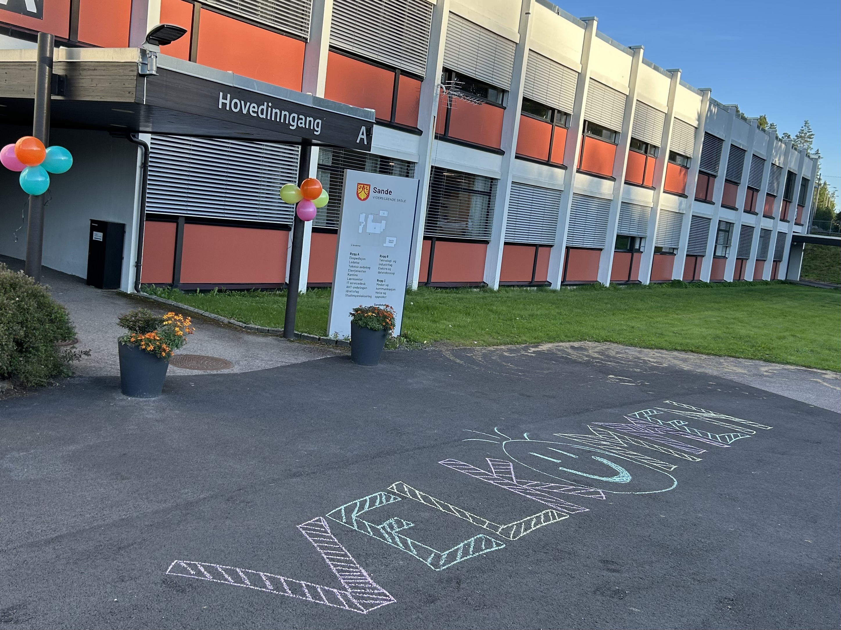 Hovedinngangen til Sande vgs med ballonger og det er skrevet "velkommen" med kritt på asfalten
