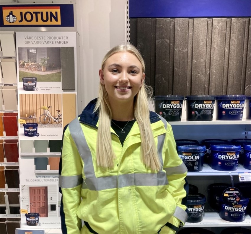 Kvinne i arbeidstøy står foran en vegg med malingsprøver.