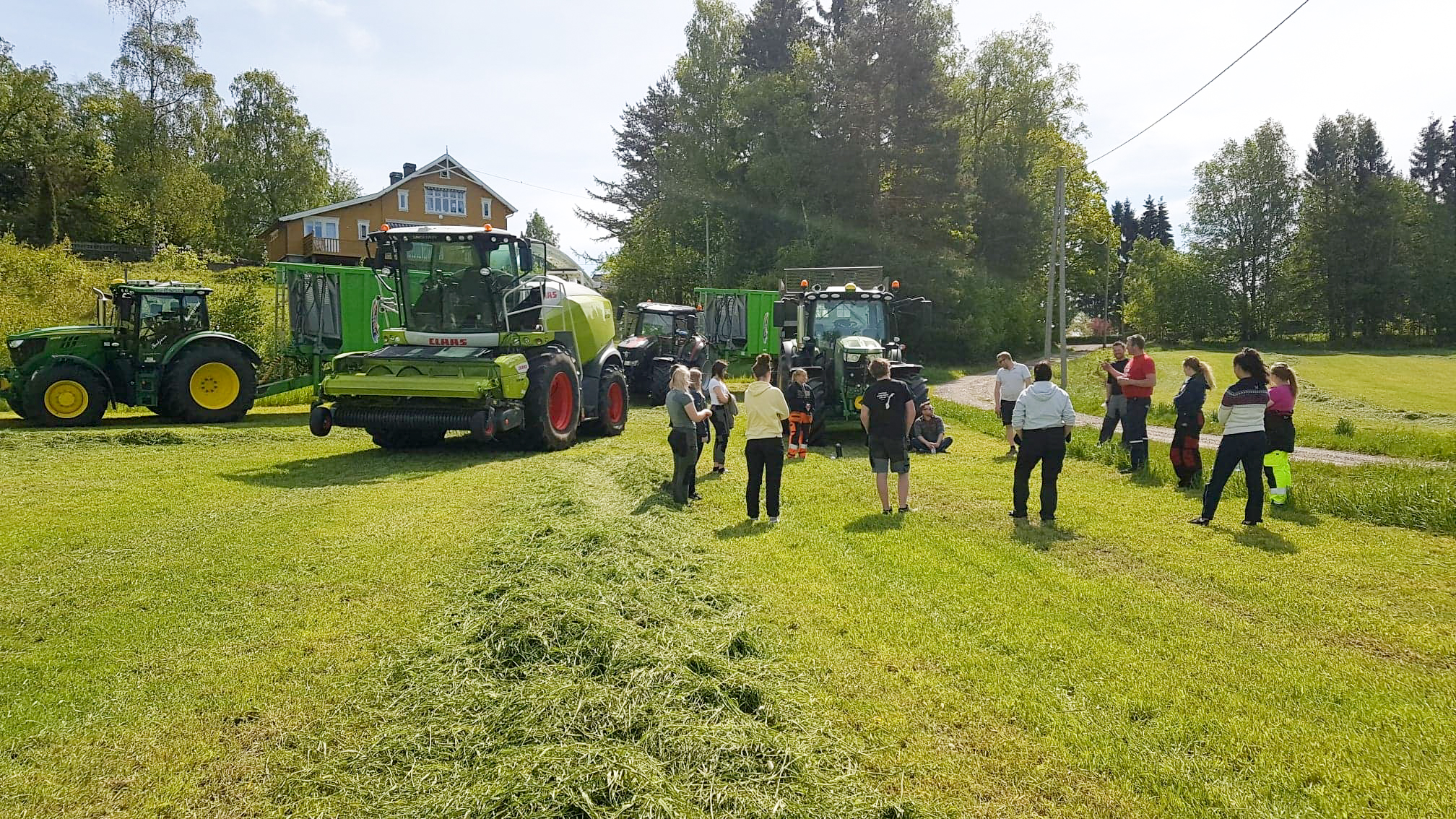 Elevene står på nyslått jorde og ser på landbruksmaskinene