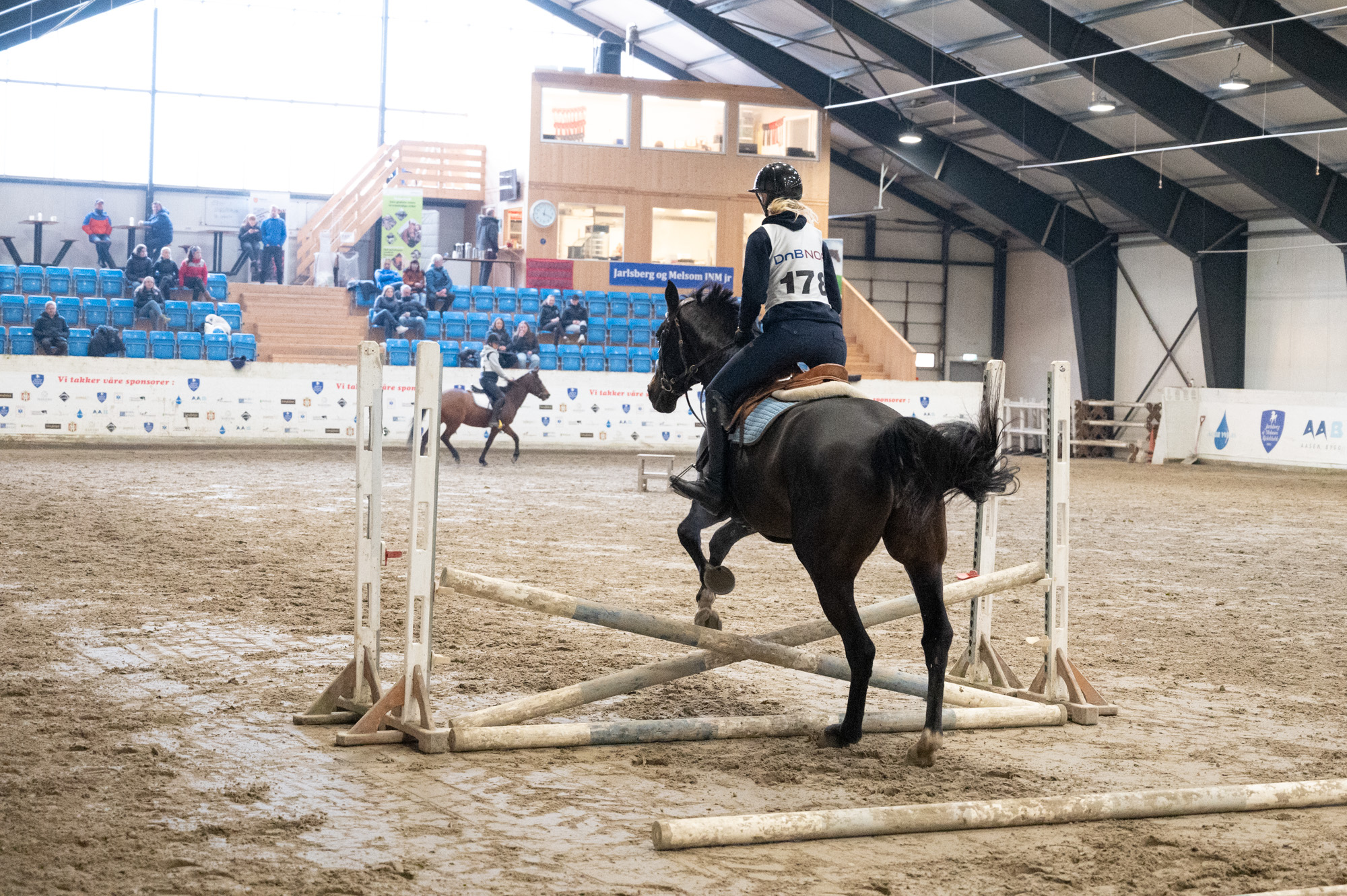 Hest og rytter hopper over hinder inne i ridehall
