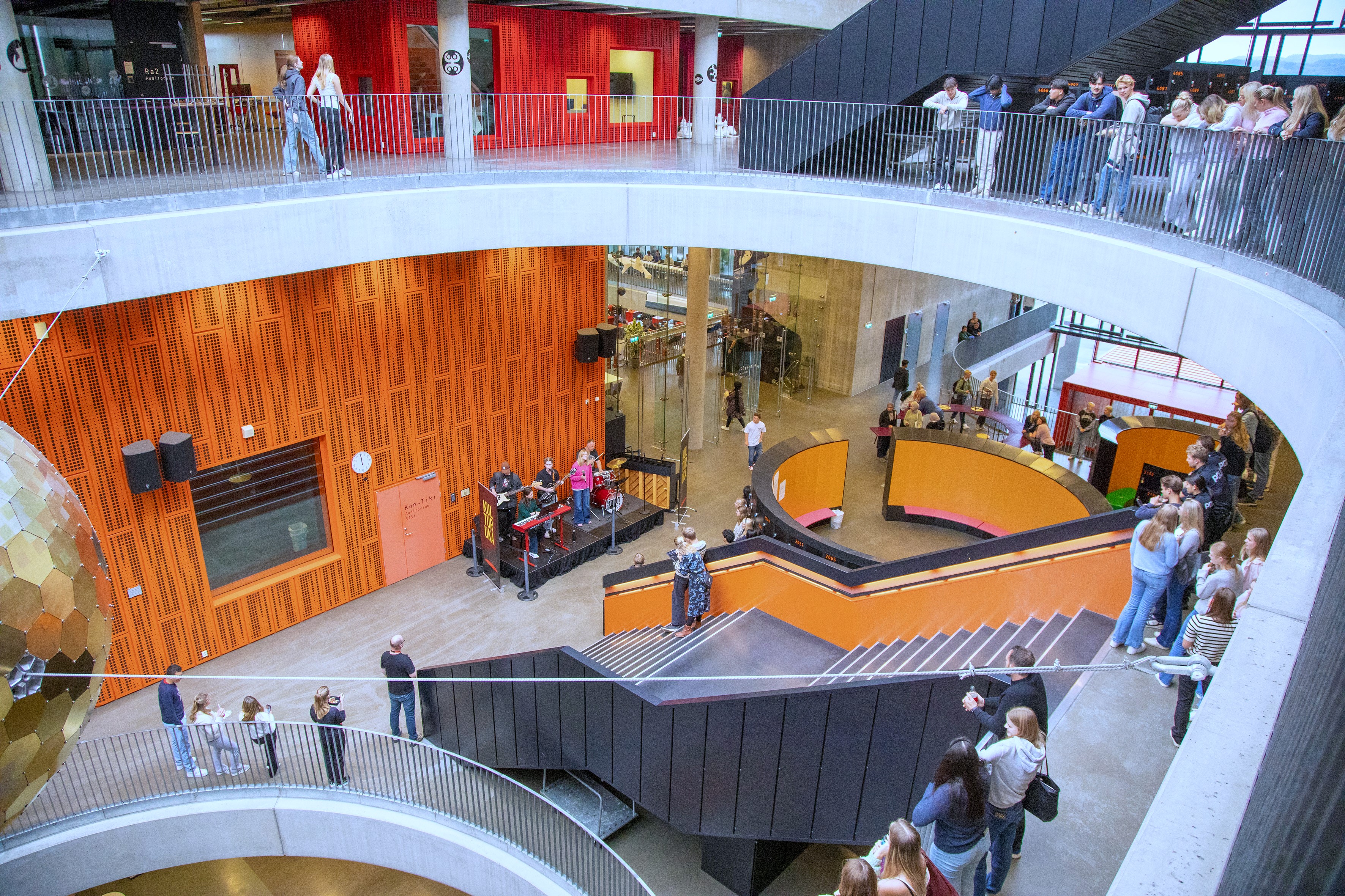 Innsiden av skolebygget. Elever står i etasjene, lent over rekkverk.