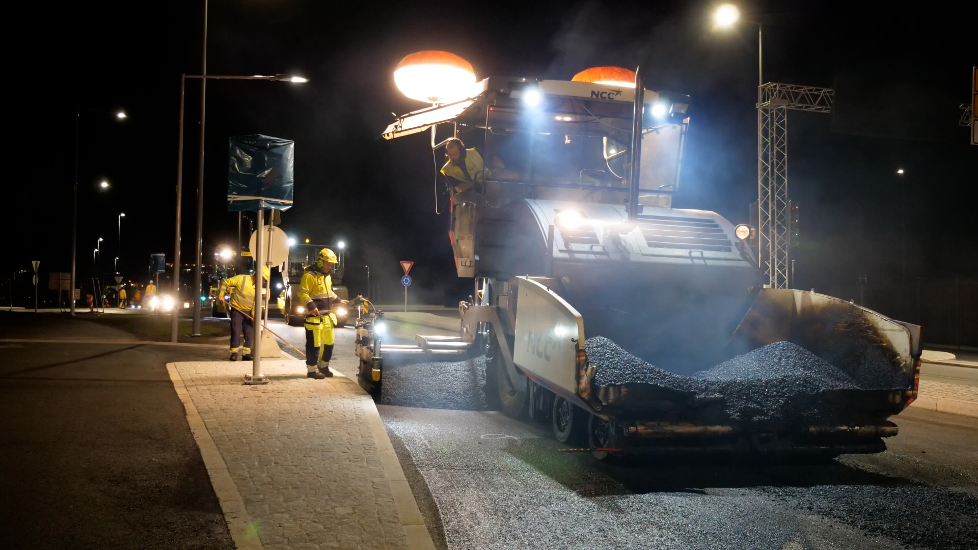 Asfaltutlegger som legger asfalt om natten, opplyst med kraftige arbeidslys.