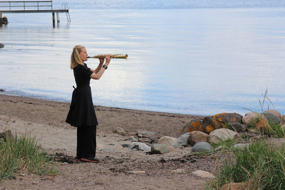 Kvinne med blåseinstrument på en strand