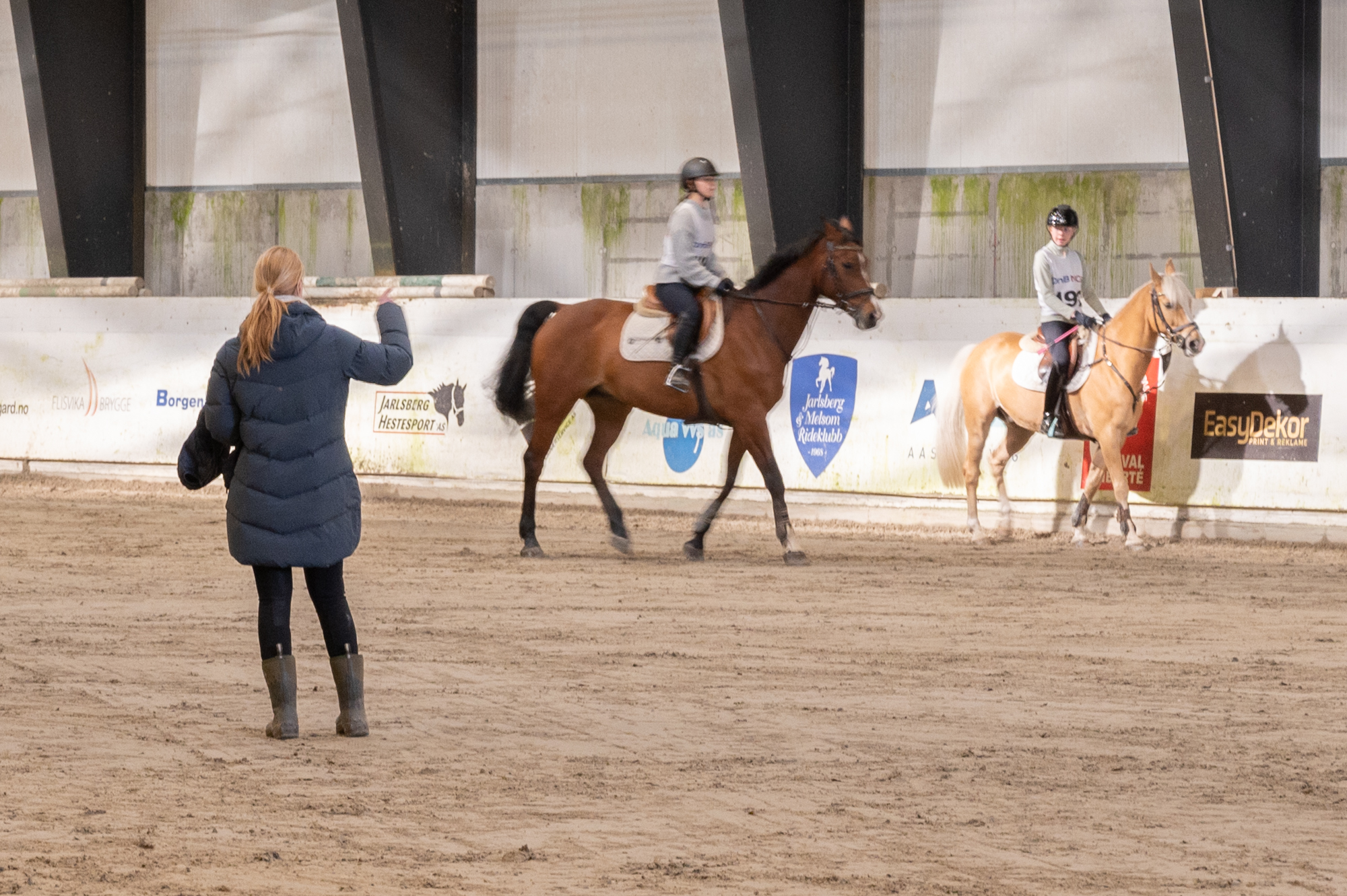 To dressurryttere og en lærer på banen i ridehallen