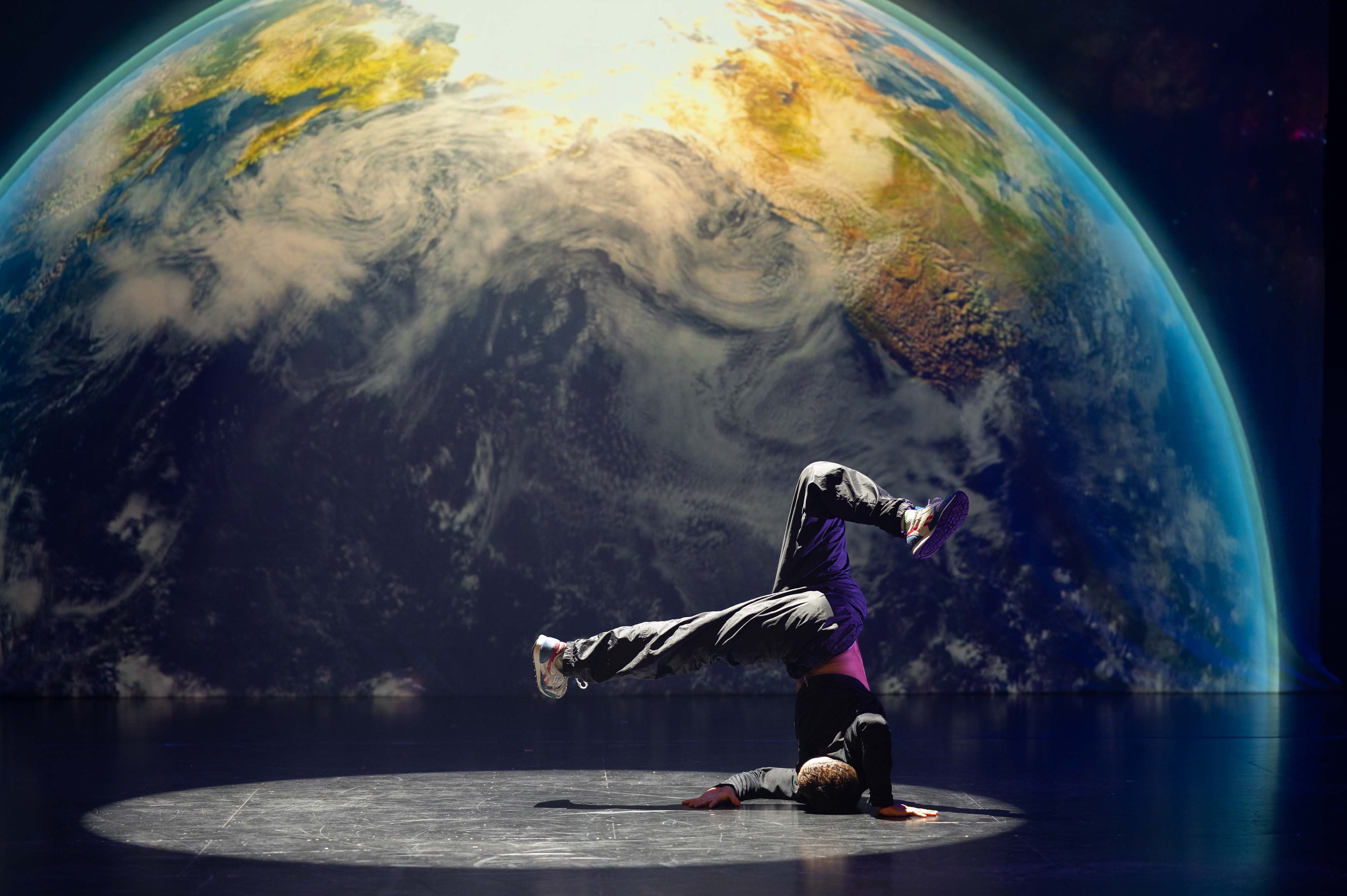 Bilde som viser en breakdanser i posisjon opp ned, med en jordklode i bakgrunnen.