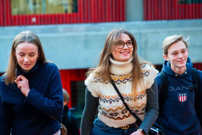 Tre smilende elever som går