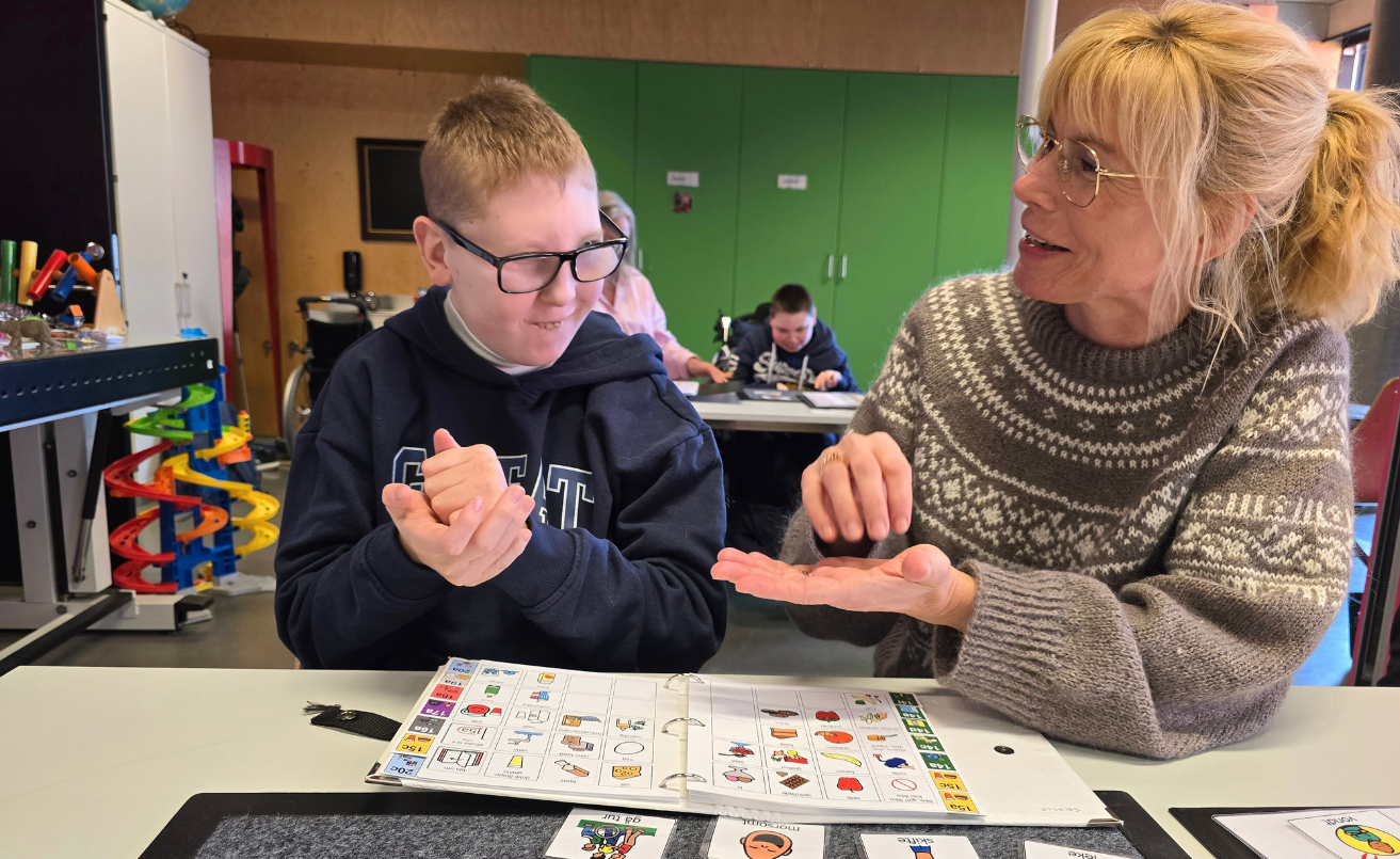 Lærer og elev med bildebok og tegn til tale.